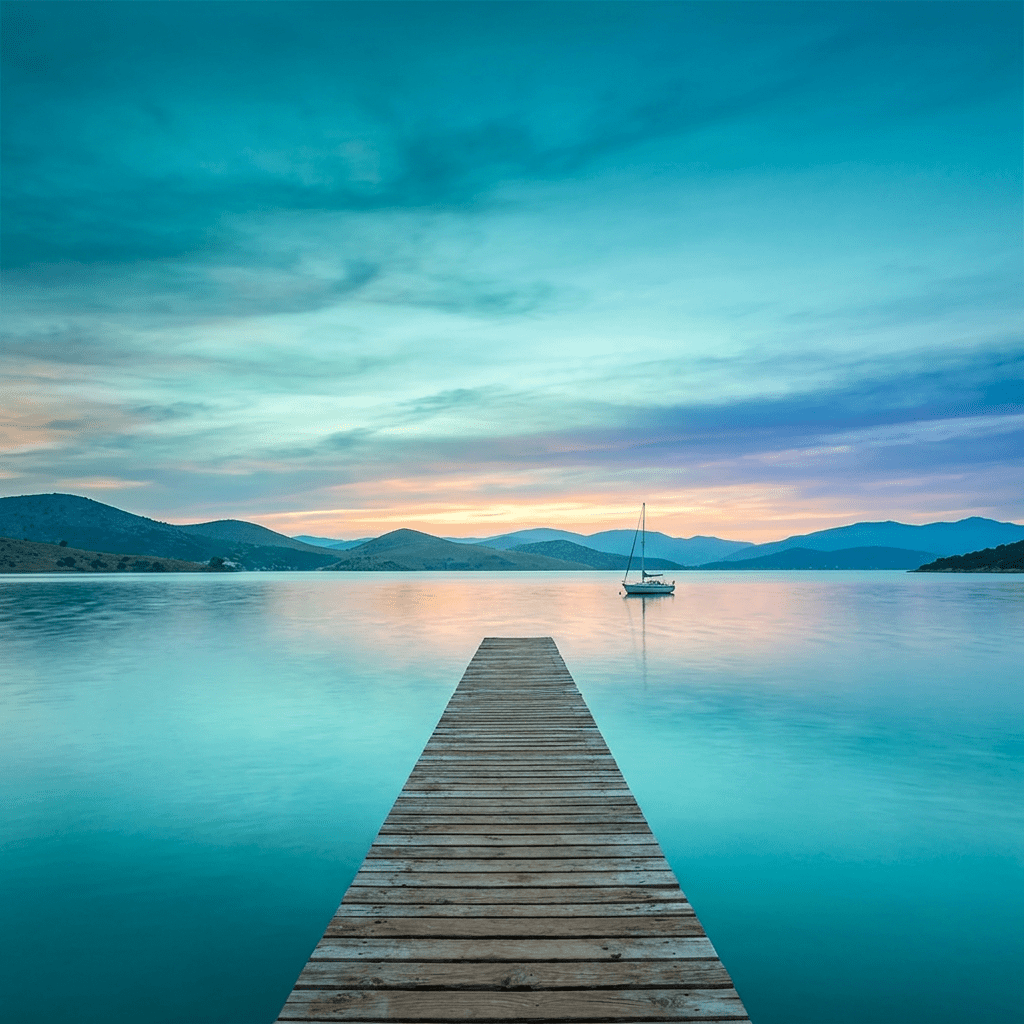 Wooden pier on calm lake water with sailboat and mountains at sunset